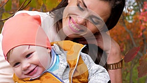 Portrait of happy family, mom near baby with drooling close-up on background of yellow trees in autumn city park