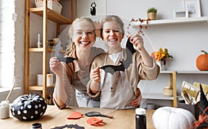 Portrait of happy family mother and cute girl daughter with cutted black paper bats in hands