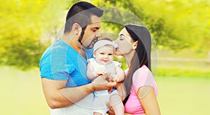 Portrait of happy family, mother and father kissing baby outdoors in summer park