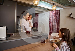 Portrait of a happy family, a single mother with two kids during breakfast in the morning at home kitchen