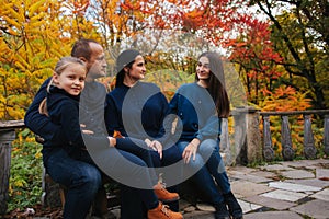 Portrait of happy family sitting on the bench in the forest. Autumn weather and colorful trees