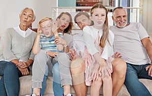 Portrait of a happy family sitting on the couch and making funny faces in the living room at home. Joyful little girl