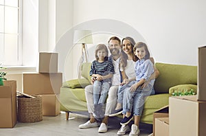 Portrait of happy family sitting on sofa between cardboard boxes in living room of their new home.