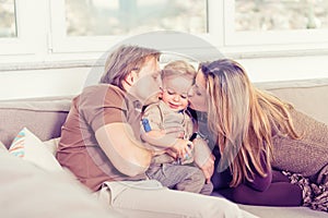 Portrait of happy family sitting on the sofa and playing. Parents kissing their baby son