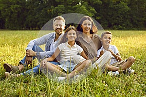 Portrait of happy family with son and daughter sitting in the summer park and looking at camera.