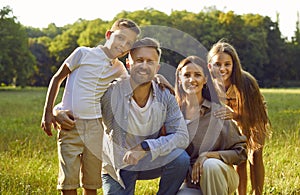 Portrait of happy family with son and daughter sitting in the summer park and looking at camera.