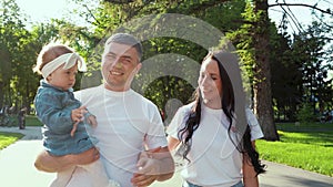 Portrait of happy family with toddler girl walking in sunny park in summer