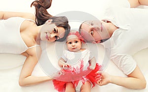 Portrait happy family together mother, father and baby lying on bed at home