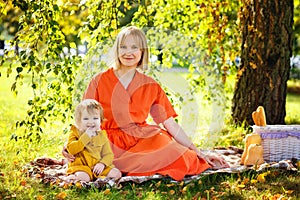 Portrait of a happy family of two. Blonde mom in orange dress and daughter enjoy a picnic in the park. Sunlight