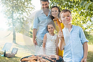 Portrait of happy family with two children standing outdoors near barbecue