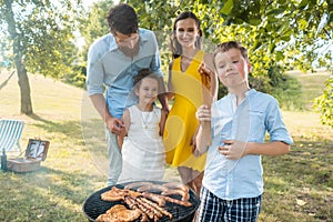 Portrait of happy family with two children standing outdoors near a barbecue