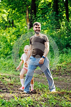 Portrait of happy family walking in park forest around trees, having fun. Little daughter keeping tight hold of father.