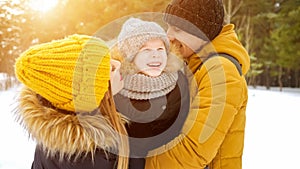 Mom and dad are cuddling and kissing their little son in winter park.