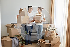 Portrait of happy family, woman and man wearing white t shirts standing with cardboard boxes, relocating to a new house, unpacking