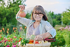 Portrait of happy farmer woman with basket of vegetables holding tomato