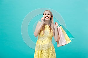 Portrait of happy fashion caucasian woman with shopping bags calling on mobile phone. on blue background.