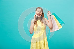 Portrait of happy fashion caucasian woman with shopping bags calling on mobile phone. Isolated on blue background.