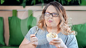 Portrait of happy fat woman eating appetizing french fries posing looking at camera