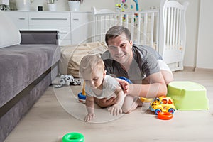 Portrait of happy father crawling with his baby boy on floor at