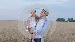 Portrait of happy father and daughter, cheerful daddy stays with merry smiling child girl on his hands in reaped wheat