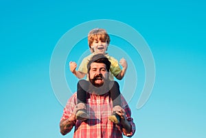 Portrait of happy father giving son piggyback ride on his shoulders. Cute boy with dad playing outdoor. Kid son hugging