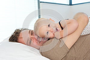 Portrait of a happy father lying down in bed and hugging cute baby