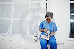 Portrait of happy female african american young doctor pediatrician in blue uniform coat and stethoscope with books at hands.