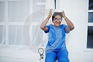 Portrait of happy female african american young doctor pediatrician in blue uniform coat and stethoscope with books at hands.