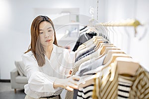 portrait of happy female asian entrepreneur working in her modern store with womenswear clothes, young chinese woman