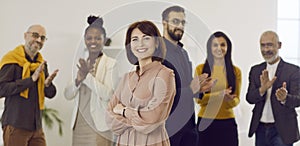 Portrait of happy female business leader with team of colleagues applauding in background