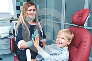 Portrait of happy female dentist and smiling young boy sitting in dental chair giving high five after teeth examination in