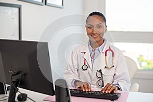 Portrait of happy female doctor sitting at computer and smiling