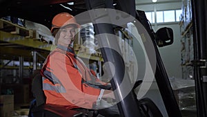 Portrait of happy female forklift truck driver looks at camera and smiles in warehouse