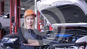 Portrait of happy female mechanic while working in car repair shop near automobile with open hood