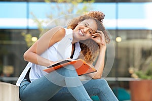 Happy female student laughing outside with pen and book photo