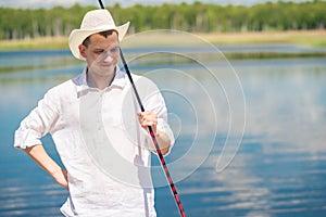 Portrait of a happy fisherman in a white hat on a lake