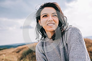 Portrait of happy and funny brunette woman smiling and looking away, against nature meadow and overcast background with windy hair