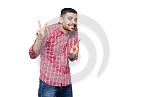 Portrait of happy funny handsome bearded young man in red checkered shirt standing and looking at camera with victory or peace