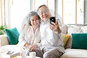 Portrait of a happy funny senior couple sitting on sofa and taking selfie at smartphone, Mature retired people having fun with new