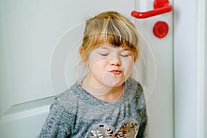 Portrait of happy funny smiling toddler girl indoors. Little preschool child with blond hairs looking at the camera.
