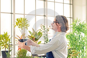 Portrait of happy gardener senior man wearing glasses holding small tree in plant pot as a hobby of home gardening at home