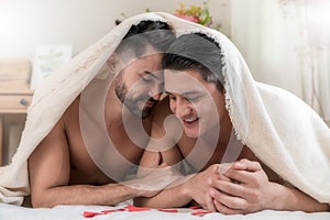 Portrait of a happy gay couple lying under a blanket on the bed together