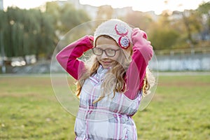 Portrait of a happy girl 7 years old, in a knitted hat, glasses, autumn sunny background