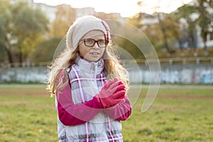 Portrait of a happy girl 7 years old, in a knitted hat, glasses, autumn sunny background