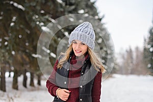 portrait of a happy girl in a blue hat, sweater and vest, stands on a snowy winter alley