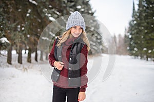 portrait of a happy girl in a blue hat, sweater and vest, stands on a snowy winter alley