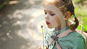 Portrait of happy girl. Child is smiling in spring day. Kid is enjoying spring. Sunny day. Blonde girl is blowing