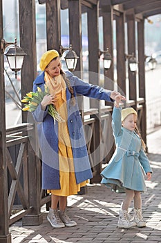 Portrait of a happy girl with mom and a bouquet of yellow tulips on a walk in spring. Flowers for International