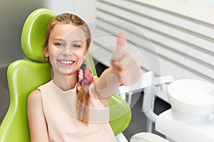 Portrait of happy girl shows thumb up gesture at dental clinic photo