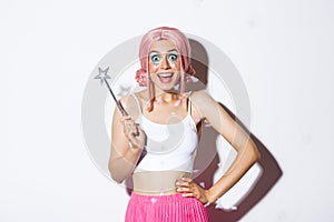 Portrait of happy girl smiling, celebrating halloween in fairy costume, with pink wig and bright makeup, holding magic